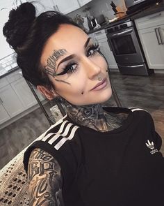 a woman with tattoos on her face sitting in a kitchen