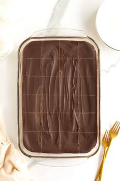 chocolate frosted cake in a pan on a white table with gold utensils