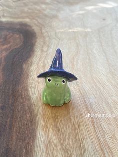 a small green figurine with a black hat sitting on top of a wooden table