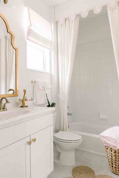 a white bathroom with pink accents and gold accessories on the sink, toilet, tub, and shower curtain