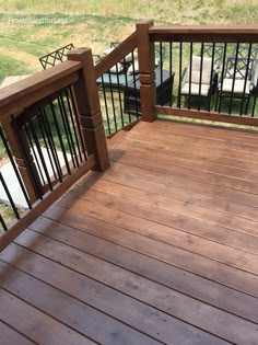 a wooden deck with metal railings and chairs on the other side, overlooking a grassy area