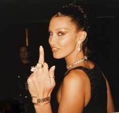 a woman in a black dress pointing to the side with her finger up and wearing gold jewelry