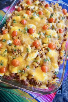 a casserole dish with meat, cheese and tomatoes in it on a colorful cloth