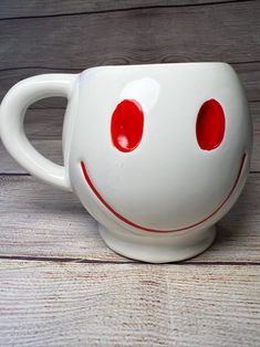 a white coffee cup with red eyes is on the wooden floor and looks like a smiley face