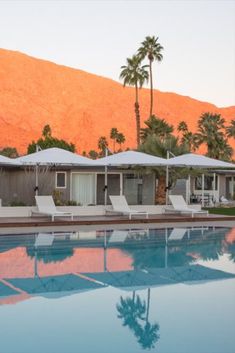 an outdoor swimming pool with chaise lounges and palm trees in the background at sunset