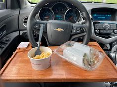 a wooden tray with food on it next to a steering wheel and dash board in a car