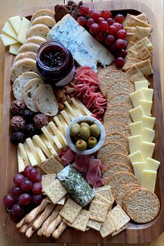 a wooden platter filled with cheese, crackers, grapes and other food items