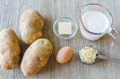 potatoes, eggs, cheese and milk on a wooden table with a measuring cup next to them