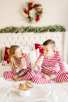 two children in matching red and white pajamas sitting on a bed with christmas wreaths