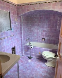 a bathroom with a toilet, sink and bathtub in purple tiles on the walls