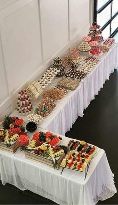 an assortment of desserts are displayed on a long table with white draping