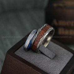 a wooden ring with silver and blue stripes on it sitting on top of a box