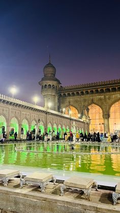 people are standing around in the courtyard of an old building with green lights on it