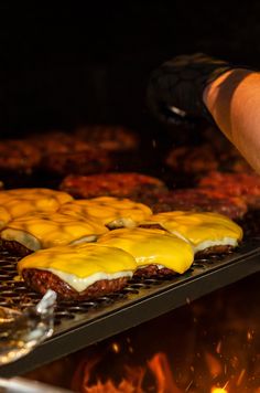 hamburgers are being cooked on the grill with yellow sauce and melted cheese over them