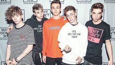 four young men standing together in front of a wall