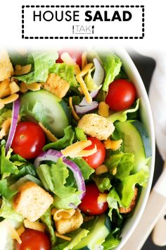 a white bowl filled with lettuce, tomatoes and croutons on top of a table