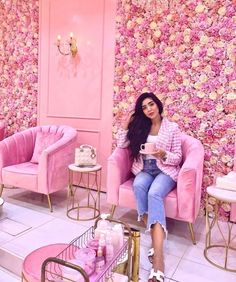 a woman sitting on a pink chair in front of a floral wall