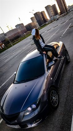 a woman sitting on top of a car in the middle of an empty parking lot