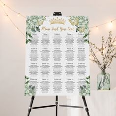 a table plan with flowers and greenery on it in front of a string of lights