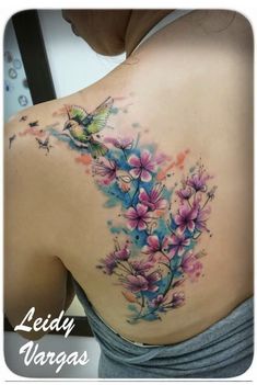 the back of a woman's shoulder with flowers and a bird tattoo on it