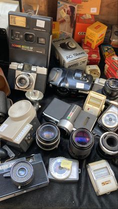 an assortment of old cameras sitting on top of a black cloth covered table next to boxes