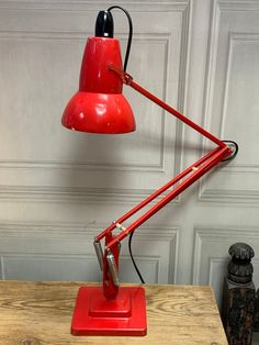 a red desk lamp sitting on top of a wooden table next to a white wall