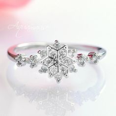 a snowflake ring is shown on top of a white surface with pink flowers in the background