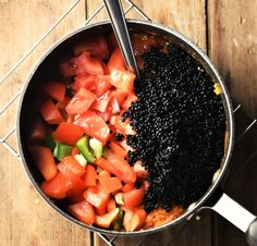 a pot filled with lots of food on top of a wooden table next to a spoon