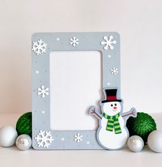 a snowman frame sitting on top of a table next to christmas balls and ornaments