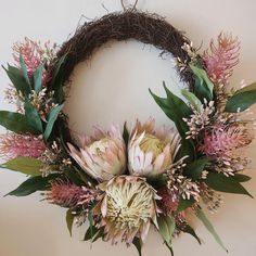 a wreath with pink flowers and greenery hanging on the wall next to a white wall