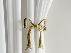 a gold bow curtain tie hanging on the side of a white drapes in front of a window