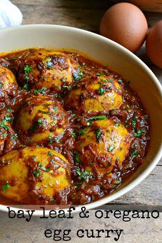 an egg curry in a white bowl next to eggs on a wooden table with the words, bay leaf & oregano egg curry