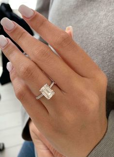 a woman's hand wearing a ring with an emerald stone in the middle and diamond band