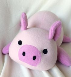 a pink stuffed pig laying on top of a white sheet with black eyes and nose