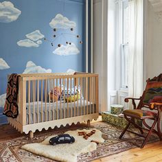 a baby's room decorated in blue and white with clouds painted on the wall