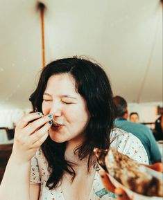 a woman sitting at a table with food in her hand and eating something out of her mouth