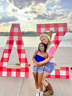 two girls hugging each other in front of a large letter