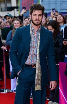 a man in a suit and tie standing on a red carpet with his hands in his pockets