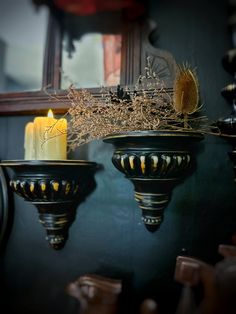 two black vases with candles in them on a table next to a mirror and wall