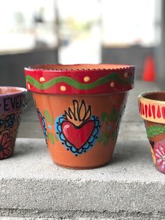 three flower pots with designs painted on them sitting on a stone ledge next to each other