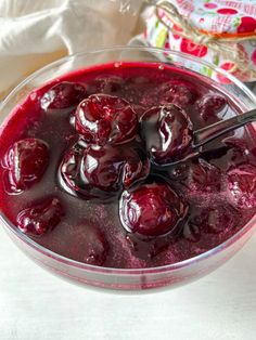 a glass bowl filled with cherries on top of a white table next to a napkin