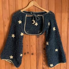 a blue sweater with white stars on it is hanging on a wooden wall next to a hanger