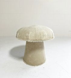 a white fur covered stool sitting on top of a floor next to a brick wall