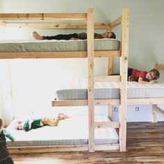 two children laying on bunk beds in a room with wood flooring and white walls