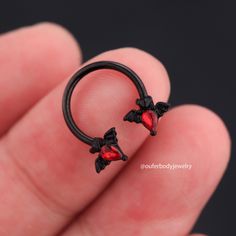 a person is holding a small ring with two bats on the outside and red crystals in the inside