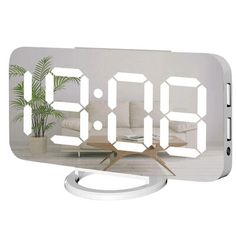 an alarm clock is sitting on top of a table next to a potted plant