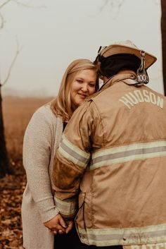 a man and woman hugging each other in the woods while wearing fire fighter gear on their back