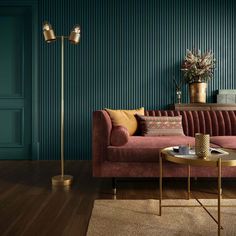 a living room with green walls and wooden flooring, a pink velvet couch in front of a gold coffee table