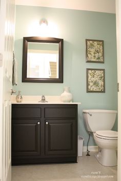 a white toilet sitting under a bathroom mirror next to a wooden sink vanity with two framed pictures on the wall