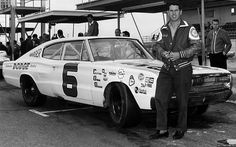 a man standing next to a race car in front of a gas station with other cars